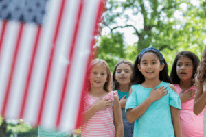 Asian girl recites Pledge of Allegience to American flag with friends