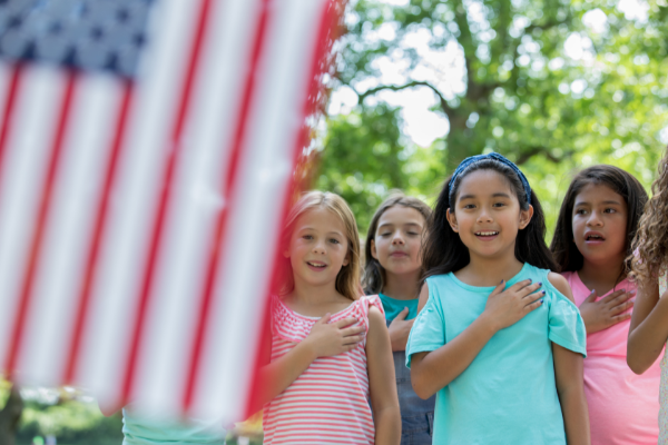 Asian girl recites Pledge of Allegience to American flag with friends